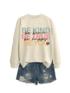 Close-up of beige crewneck sweatshirt with 'BE KIND' print and side slit hem detail