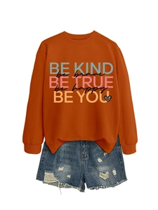 Flat lay of an orange 'Be Kind' sweatshirt paired with blue distressed denim shorts