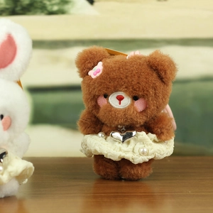 Cute plush bear keychain with lace skirt and pearl details on a wooden surface
