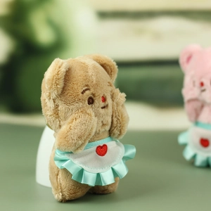 Detailed macro view of a plush bear charm featuring a white apron with heart embroidery