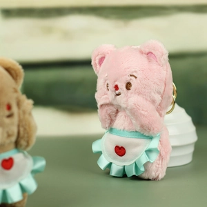 Detailed view of pink plush bear keychain wearing blue apron with red heart charm