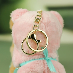 Detail of golden metal lobster clasp and keychain on soft pink plush bear pendant