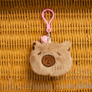 Detalle de llavero de peluche de carpincho con campana rosa y mosquetón en fondo tejido