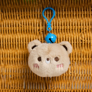 Detalle de llavero de oso de peluche marrón claro con cascabel azul y bordado fino