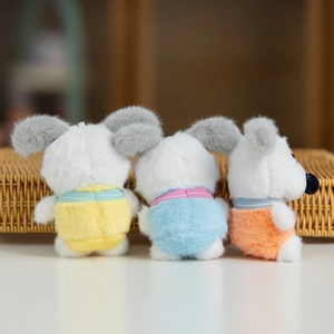 Tre ciondoli a forma di cane di peluche in tute colorate su un cesto di vimini