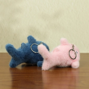 Dettaglio dei portachiavi a forma di squalo in peluche blu e rosa su legno