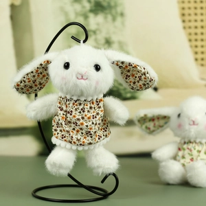 Detailed close-up of a white plush rabbit doll wearing a vintage floral dress on a stand