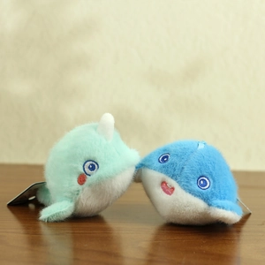 Macro detail of plush whale pendants in mint green and blue on a wooden surface