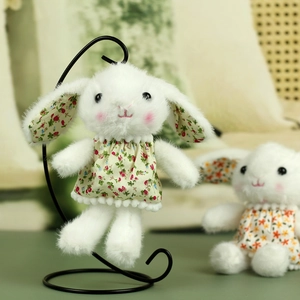 Detail of white plush bunny keychain in green floral dress hanging on a black metal stand