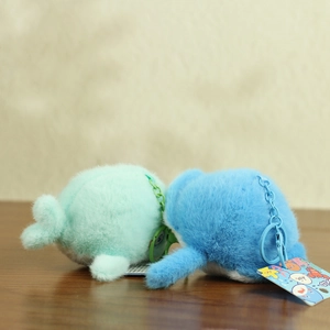 Detail of plush whale keychains in mint green and royal blue on a wooden table