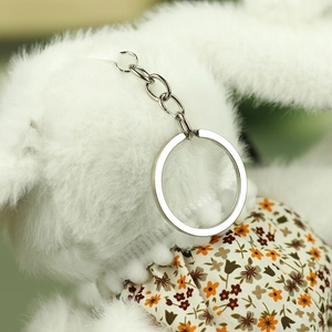 Macro detail of a soft white plush rabbit pendant wearing a floral dress with silver keychain