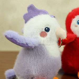 Close-up of a purple and white plush bird keychain with embroidery and metal ring