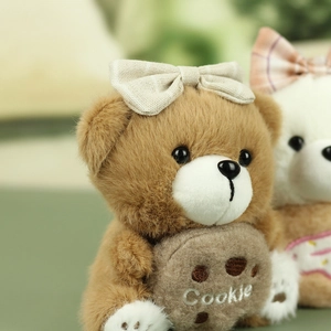 Détail d'un ours en peluche marron avec broderie Cookie et nœud à carreaux clair