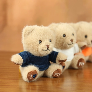 Three plush teddy bear keychains in soft brown fur wearing blue white and orange shirts