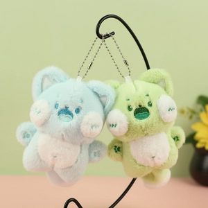 Close-up of soft blue and green plush cat keychains with embroidered details on metal stand