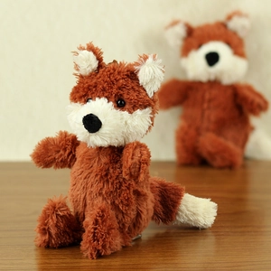 Cute reddish-brown plush fox keychain with fluffy tail on a warm wooden background