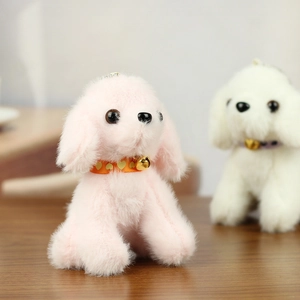 Close-up of cute plush teddy dog keychains in pink and white with golden bells