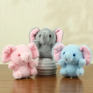 Soft plush elephant keychains in pink, grey and blue colors on a wooden surface