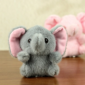 Close-up of a mini plush elephant toy with gray fur and pink ears on wood surface