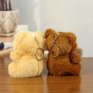 Cute beige and brown plush bear keychains with metal rings on a wooden tabletop