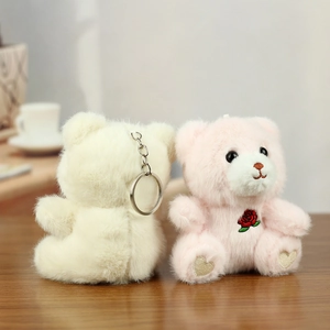 Close-up of pink and white plush teddy bear keychains with rose embroidery on a table