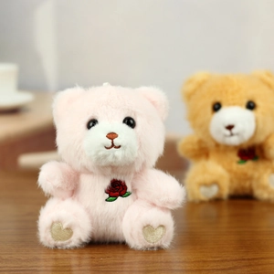 Close-up of plush bear pendants with heart embroidery on feet and a red rose