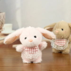Close-up of pink plush bunny with red plaid lace bib on a rustic wooden surface
