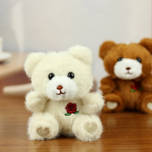 Detailed close-up of cute teddy bear plush keychain with rose embroidery on natural wood