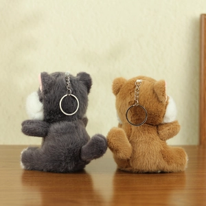 Rear view of fluffy plush cat keychains in dark grey and caramel brown on wood table