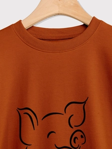 Close-up of ribbed crew neck and cute pig graphic on brown cotton sweatshirt