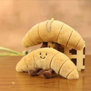 Cute croissant plush keychain charms with smiling faces on a warm wooden background