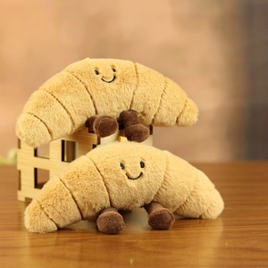 Detail of two plush croissant toys with cute embroidered faces on a wooden shelf