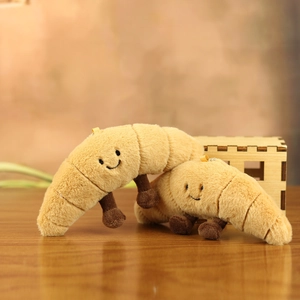 Close-up of cute plush croissant keychains with smiling faces on a warm wooden background