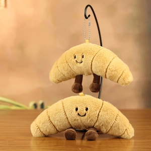Close-up of cute plush croissant keychain with embroidered smile and metal ball chain