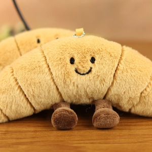 Detailed view of plush croissant keychain with embroidered smiley face and metal chain