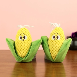Close-up of two plush corn toys with textured yellow kernels and green husks on wood