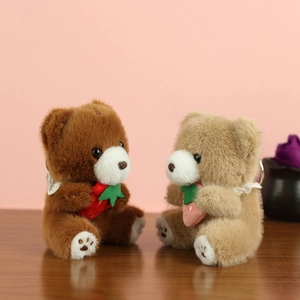 Detail of plush bear keychains with lace collars holding strawberries on wood surface
