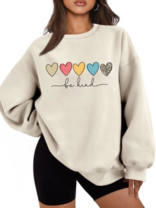 Détail de l'inscription be kind et des cœurs imprimés sur le sweat-shirt crème