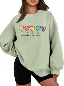 Détail d'un sweat vert clair avec texte 'be kind' et motifs de cœurs colorés