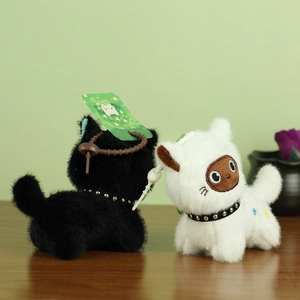 Close-up of black and white plush cat charms with rivet collars and tags on wood desk