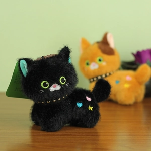 Close-up of black plush cat keychain with embroidered hearts and green eyes details