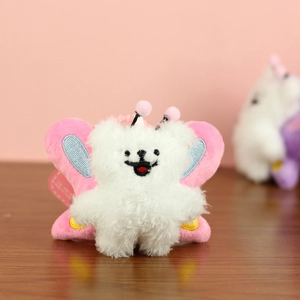 Close-up of white plush bear keychain with pink butterfly wings on wooden background