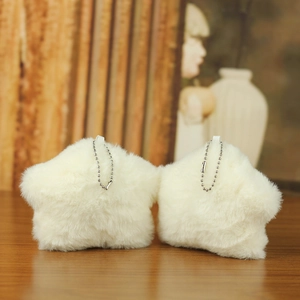 Detailed view of two white star-shaped plush charms with silver chains on wood surface