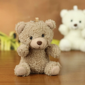 Close-up of curly brown teddy bear keychain with silver chain on wooden desk