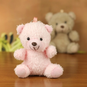 Close-up of pink curly plush teddy bear keychain with silver bead chain on wood surface