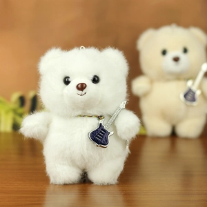 Close-up of white plush teddy bear keychain featuring a blue guitar charm and soft texture