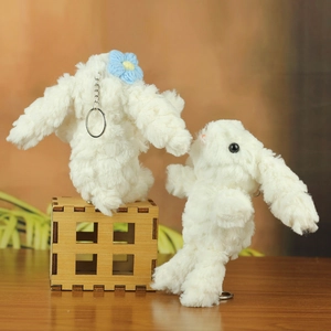 Close-up of fluffy white rabbit plush keychains with metallic chains and a blue knit flower