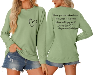 Détail du sweat-shirt vert sauge avec texte au dos et motif cœur sur tissu côtelé