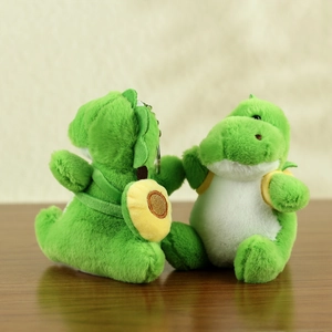 Detail of two plush green dinosaur keychains with small yellow bags on wooden surface