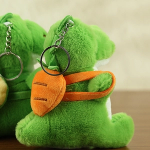Close-up of green plush dinosaur pendant with orange carrot backpack and metal keychain